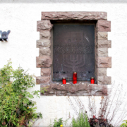 Die dunkle Metallplatte ist in eine weiße Mauer eingelassen und wird von Bruchsteinen umrahmt. Die Inschrift der Gedenktafel lautet: Hier stand bis zur Zerstörung durch die Nationalsozialisten am 9.11.1938 die Synagoge der Jüdischen Gemeinde Honnef“. Auf dem Mauervorsprung vor der Tafel stehen drei rote Friedhofskerzen.