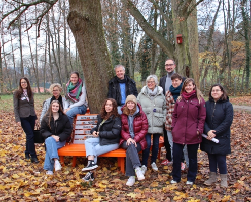 Park mit Baum und orange Bank: Schülerinnen, sitzend und Personen stehend