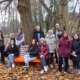 Park mit Baum und orange Bank: Schülerinnen, sitzend und Personen stehend