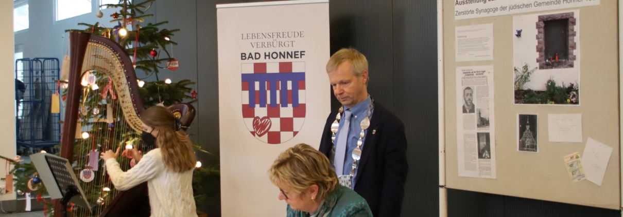 Sylvia Löhrmann sitzend mit Stift, Bürgermeister Otto Neuhoff stehend und Harfenspielerin