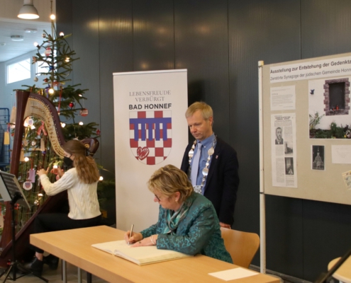 Sylvia Löhrmann sitzend mit Stift, Bürgermeister Otto Neuhoff stehend und Harfenspielerin