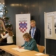 Sylvia Löhrmann sitzend mit Stift, Bürgermeister Otto Neuhoff stehend und Harfenspielerin
